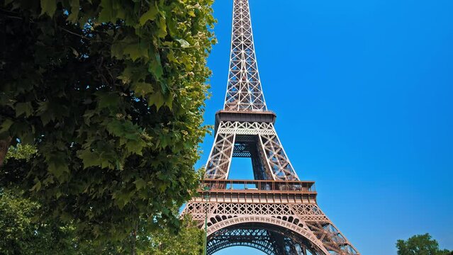 Close-up view of the historical landmark in Paris. Amazing view of the Tour between green trees of the World famous symbol of Paris on a sunny day.