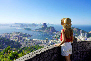 Fototapeta na wymiar Tourism in Rio de Janeiro. Back view of traveler girl enjoying sight of famous Guanabara Bay with Sugarloaf Mountain in Rio de Janeiro, UNESCO World Heritage, Brazil.