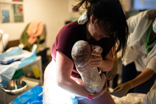 Woman grabbing newborn baby after giving birth in maternity ward