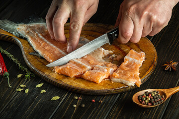 Cutting and slicing fresh fish on a cutting board by the hands of a cook. Homemade delicious fish dish according to an old recipe with the addition of spices and pepper.