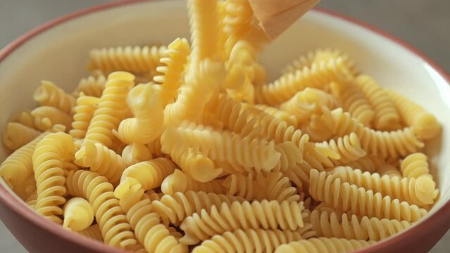 Raw Fusilli pasta falling into a bowl, slow motion