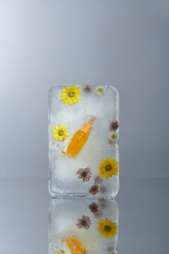 Serum in glass bottle and fresh flowers frozen in a piece of ice