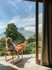 Woman relaxing in a chair on a balcony with mountain views - 620660295