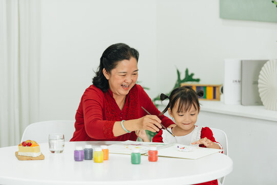 Happy grandmother and child drawing with watercolor together at table