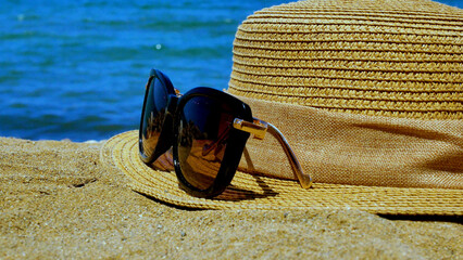 Sunglasses and a straw hat on the sand against the background of the sea. The concept of recreation...