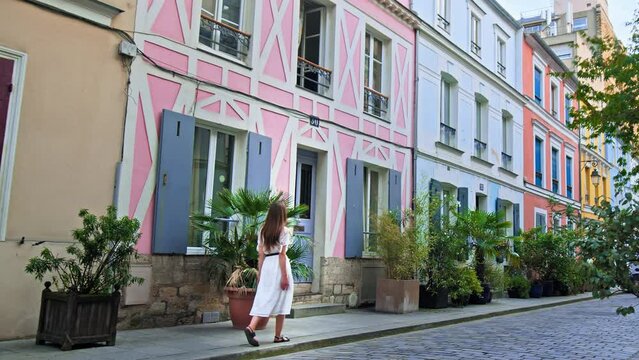 A beautiful woman in a dress visits a Parisian street with colorful houses in Paris, France. Female tourist explore a Unique French street popular destination for filming and for social media photos.