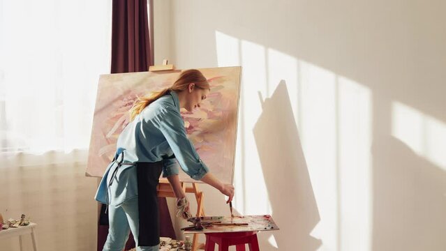 Female Works on Abstract Oil Painting, Using Paint Brush She Creates Modern Masterpiece. Painting technique, painters concept. Artist mixing oilcolor on palette. Girl painting a picture. Slow motion.