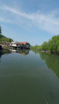Vertical video. Flying close Asian village embankment boat calm water river local rural house green forest aerial view. FPV sport drone close low shot tropical landscape port harbor fishing ship sunny