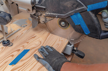The process of cutting a wooden board with a circular saw. A carpenter's hand in a glove.