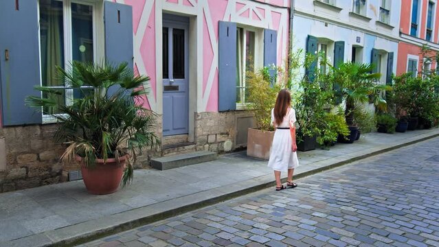 A beautiful woman in a dress visits a Parisian street with colorful houses in Paris, France. Female tourist explore a Unique French street popular destination for filming and for social media photos.