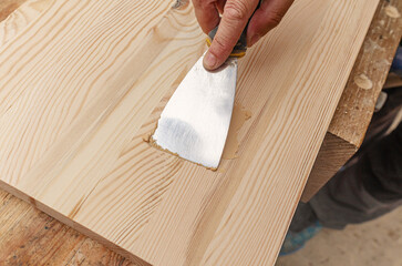 Covering knots on a wooden board with putty. Spatula, putty, wooden board. Carpenter's hands.