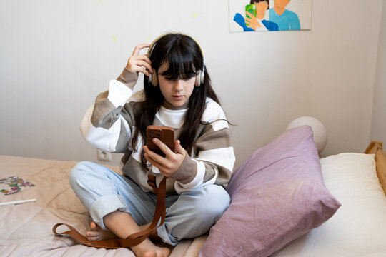 Teen Girl Chilling With Smartphone and headphones On Bed