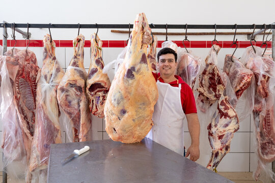 Proud worker of butchery holding meat carcass and smiling at camera