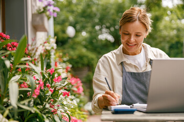 Beautiful flower shop owner wearing apron working on laptop in her store