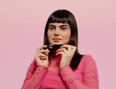 Woman choosing a long stay mascara over pink background