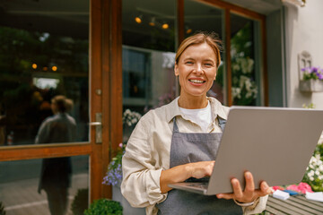 Obraz premium Beautiful flower shop owner wearing apron working on laptop in her store