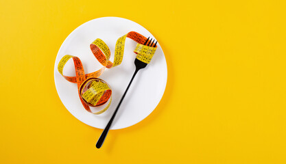Diet, Weight Loss Concept, Empty Plate with Measuring Tape and Fork Over Bright Yellow Background