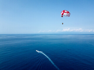 The motorboat darts swiftly across the surface of the sea, dragging a colorful parachute behind it....