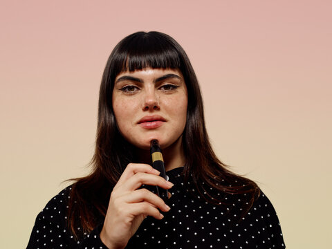 Woman wearing black jacket and holding makeup product pink backgroound