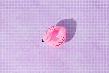 Flamingo float in bright sunlight against pink tiles.