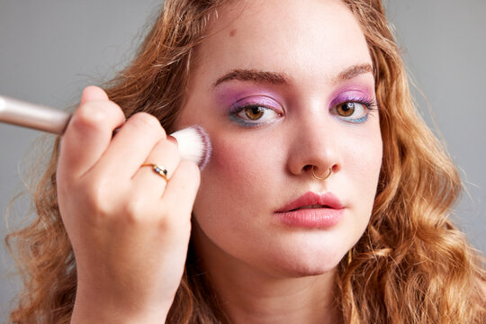 Young female applying blush on cheeks