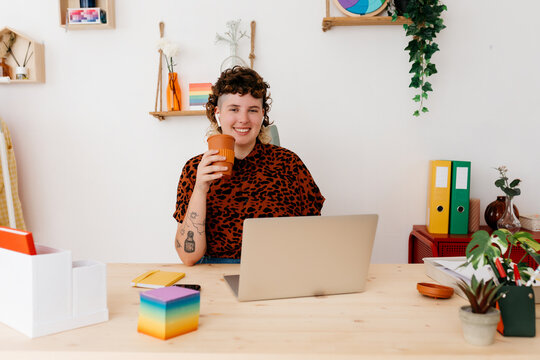 Happy non binary person with cup of coffee and laptop - Powered by Adobe