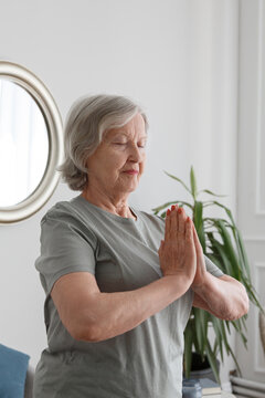 Aged woman practicing yoga with hands in namaste