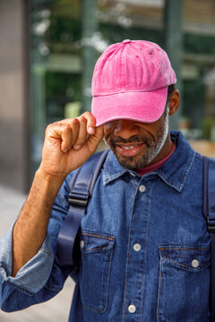 Man in denim jacket holding visor of his pink cap on a sunny day