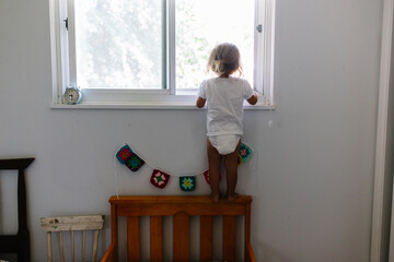 Toddler girl stands on back of bed to look outside