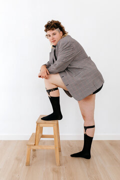 Stylish young queer leaning on knee with foot on stool
