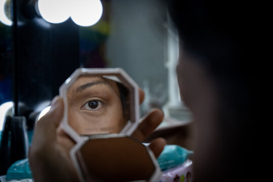A transgender woman finishes her eye makeup in a compact mirror