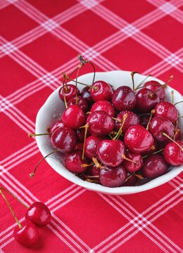 Ripe juicy cherries with water drops in a ceramic bowl on a table with a red tablecloth. Summer berries.