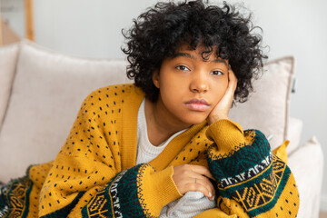 African american sad thoughtful pensive unmotivated girl sitting on sofa at home indoor. Young...