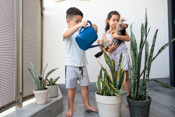 Smiling Girl Holds Dog, Boy Cares for Flowers with Blue Watering Can, At Joyful Summer Day. © Inna