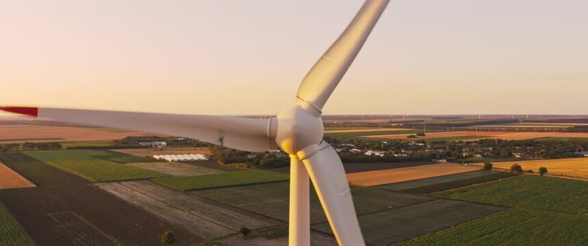 Close up Front view Wind turbine spinning blades on sunset at farm fields landscape. Renewable energy production. Aerial anamorphic view 2.36:1 Slow camera zoom out