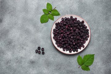 Black raspberries in a bowl on a gray concrete background. View from above, flat lying.