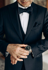 A man in a classic suit and bow tie controls the time by looking at his watch. A successful man is...