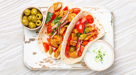 Traditional Greek Dish Gyros: Pita bread Wraps with vegetables, meat, herbs, olives on rustic wooden cutting board with Tzatziki sauce, olive oil top view, white wooden summer background.