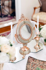 A round mirror in oriental style and lighted candles stand on the table close-up. A beautiful table mirror and candlesticks with oriental ornaments decorate the living room