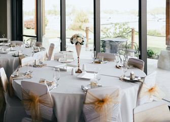 Round serving table in a restaurant decorated with flowers. Restaurant with festive decoration in the form of flowers and ribbons. Preparing for the wedding party and reception