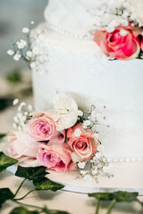 Beautiful white cake decorated with red roses and confectionery patterns. Cake for a wedding or anniversary. Beautiful decoration in the form of fresh flowers for a wedding cake