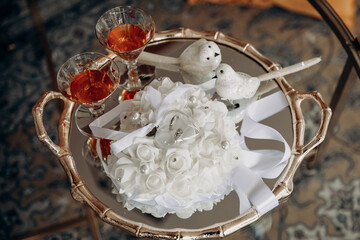Wedding rings on a white pillow and two glasses of cognac on a tray. Wedding accessory in the form of gold rings and alcohol. Wedding day and rings for the bride and groom