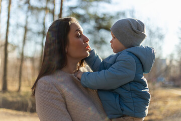 Fototapeta premium Happy family outdoor. Mother embracing her child outdoor. Mom lifting in air little toddler child son. Woman and little baby boy resting walking in park. Mother hugs baby with love care