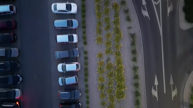 This drone footage captures a scenic view of parked cars lining the roadside, flanked by a lush green belt. The shot is accentuated by clear directional arrows on the road, guiding viewers towards th