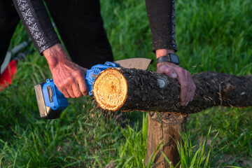 Hand-held portable camping electric saw on a battery for cutting firewood and wood. Close-up, a hand sawing a log, splinters flying
