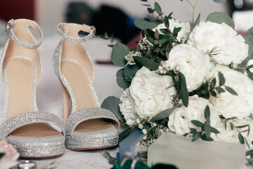 The bride's high-heeled shoes and a wedding bouquet of roses close-up. Wedding accessories in the form of shoes and a bouquet for the ceremony. Sparkling shoes of the bride and a luxurious bouquet