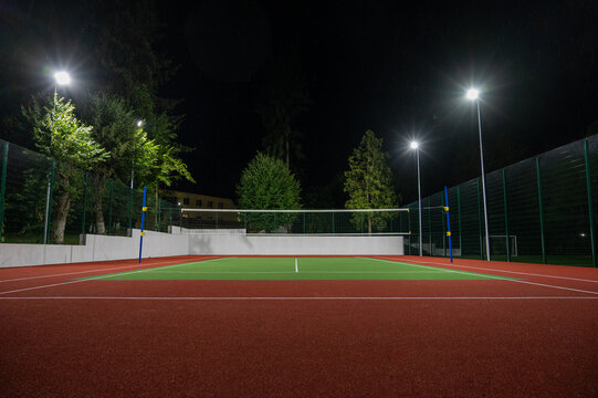 Sports volleyball field in the park with artificial grass of the stadium on the background of green trees. evening lighting with powerful lanterns, view from below