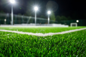 Sports field in the park with artificial grass stadium on the background of green trees. evening lighting with powerful lanterns, view from below