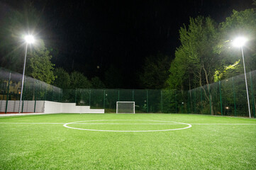 Sports field in the park with artificial grass stadium on the background of green trees. evening lighting with powerful lanterns, view from below