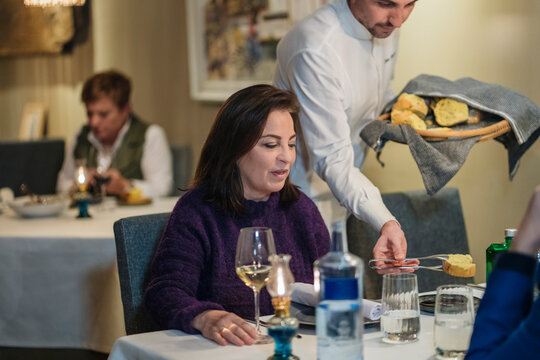 Crop waiter serving bread for customers in restaurant